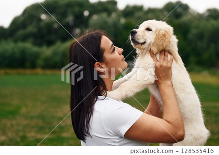 Cute little dog. Woman with golden retriever dog is on the green field 128535416