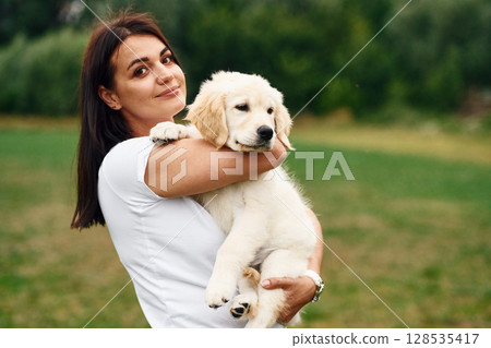 Cute little dog. Woman with golden retriever dog is on the green field Cute little dog. Woman with golden retriever dog is on the green field 128535417