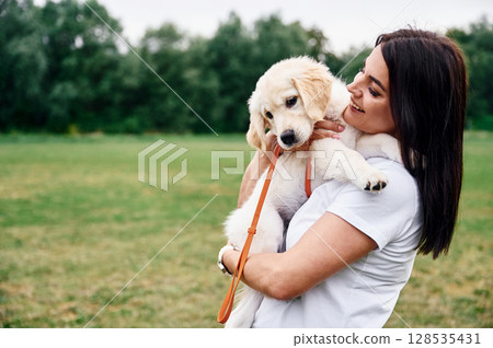 Beautiful woman with cute little golden retriever dog is on the green field Beautiful woman with cute little golden retriever dog is on the green field 128535431