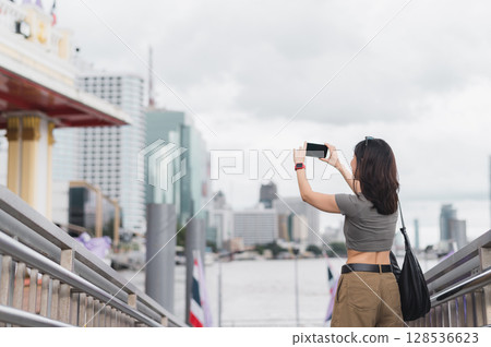Solo southeast asian woman teenager blogger express joy. world travel explorer wait to take photo with smartphone. tourism concept for local cultural experience Chao Phraya River Bangkok 128536623