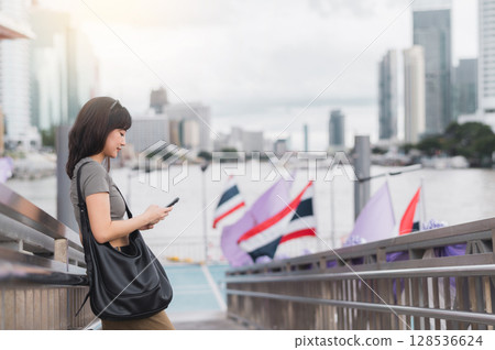 Happy young southeast asian woman and travel blogger using smartphone map searching for guide. tourism concept for local cultural experience in Bangkok Thailand by Chao Phraya river 128536624