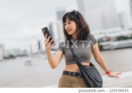 Happy young southeast asian woman teenager blogger world travel explorer using smartphone searching guide for local cultural experience. Tourism concept for Asia at Chao Phraya River Bangkok 128536635