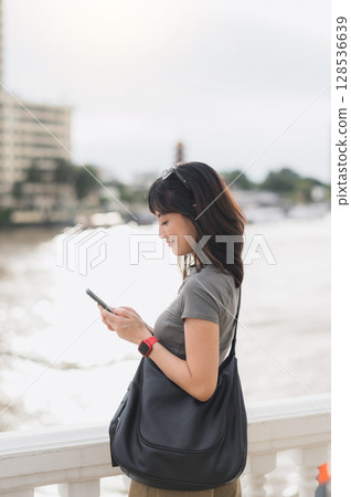 Young southeast asian woman teenager blogger searching map smartphone for local travel guide. world explorer tourism concept for cultural experience Bangkok Thailand by Chao Phraya river Asia 128536639