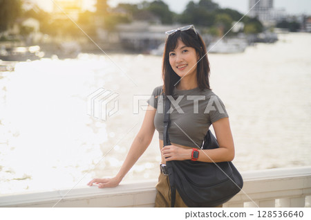 Happy young southeast asian woman or teenager blogger on solo world travel in Asia. local cultural tourism experience concept for an explorer with smartphone by Chao Phraya River Bangkok Thailand 128536640