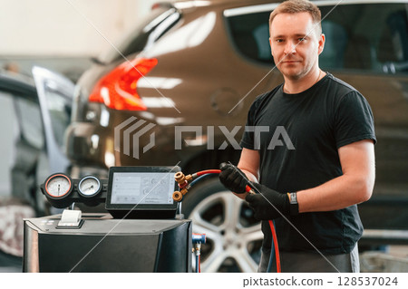 With wires in hands. Man is works in the automobile repairing salon With wires in hands. Man is works in the automobile repairing salon 128537024