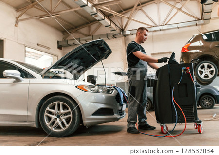 Using electric device. Man is works in the automobile repairing salon 128537034