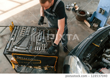 Top view of employee that standing by the toolbox. Man is works in the automobile repairing salon Top view of employee that standing by the toolbox. Man is works in the automobile repairing salon 128537040