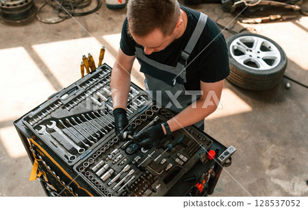 Standing by the toolbox. Man is works in the automobile repairing salon Standing by the toolbox. Man is works in the automobile repairing salon 128537052