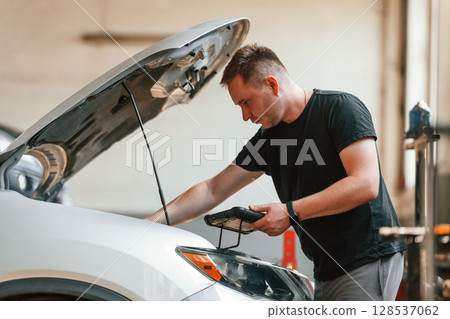 Holding the tablet. Man is works in the automobile repairing salon Holding the tablet. Man is works in the automobile repairing salon 128537062