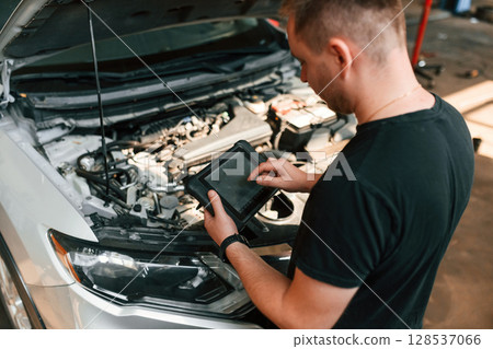 Holding the tablet. Man is works in the automobile repairing salon Holding the tablet. Man is works in the automobile repairing salon 128537066