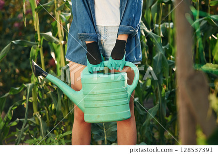 Plastic watering can in hands. Beautiful young woman is gardening 128537391