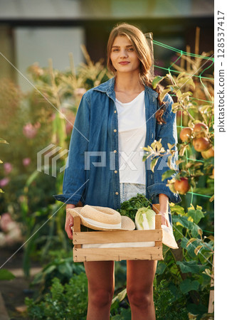 Confident worker with wooden box. Beautiful young woman is gardening 128537417