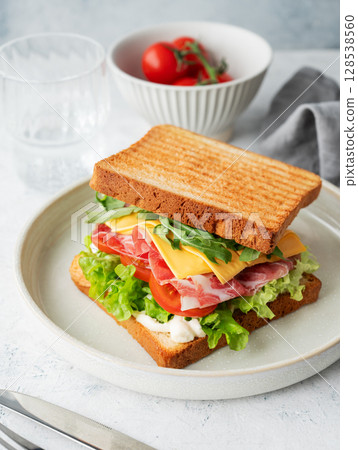 Sandwich of toast bread with bacon, cheese, tomatoes, lettuce, arugula  on a light background 128538560