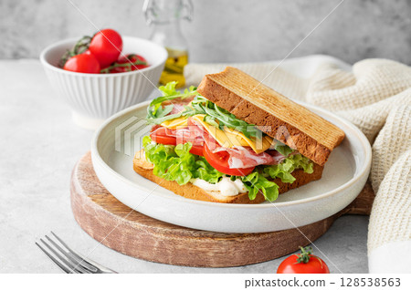 Toast club sandwich with bacon, cheese, tomatoes, lettuce, arugula and sauce  on a wooden board 128538563