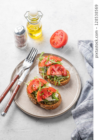 Healthy sesame toast with tomatoes, mozzarella, arugula and pesto on plate on light background 128538569