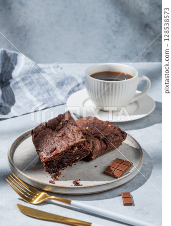 Chocolate brownie with nuts on a plate on a light background with cup of freshly brewed coffee 128538573