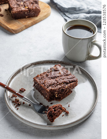 Chocolate brownie on a plate on a light background with cup of freshly brewed coffee and napkin. 128538576