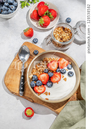 Natural yogurt with granola, blueberry and strawberry in a bowl on a wooden board  128538582