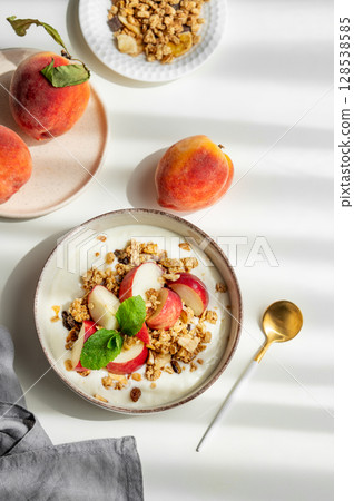 Natural greek yogurt with granola or muesli, peach and mint in a bowl on a white background 128538585