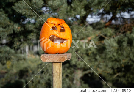 Carved Halloween pumpkin with smiling face on wooden post outdoors 128538940