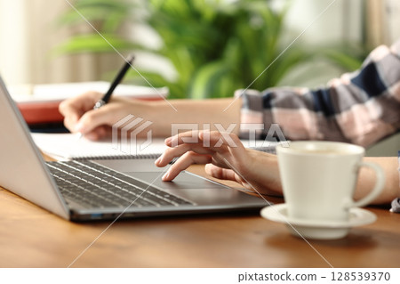 Student hands checking laptop and taking notes on wooden table 128539370