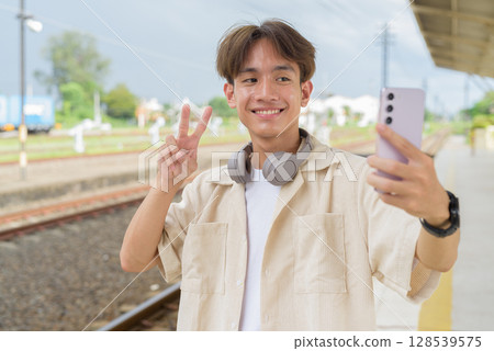 Young non binary tourist traveler in train station using phone Young non binary tourist traveler in train station using phone 128539575