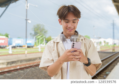 Young non binary tourist traveler in train station using phone 128539576