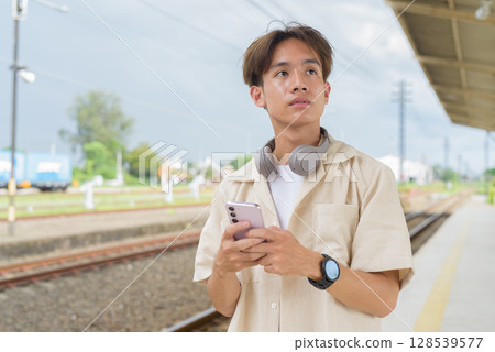 Young non binary tourist traveler in train station using phone Young non binary tourist traveler in train station using phone 128539577