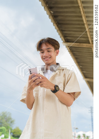Young non binary tourist traveler in train station using phone Young non binary tourist traveler in train station using phone 128539582