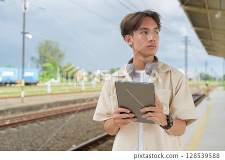 Young non binary tourist traveler in train station using digital tablet computer 128539588