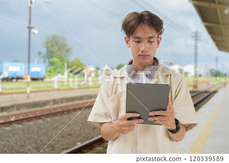 Young non binary tourist traveler in train station using digital tablet computer 128539589
