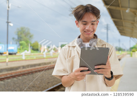 Young non binary tourist traveler in train station using digital tablet computer 128539590