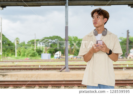 Young non binary tourist traveler in train station using phone Young non binary tourist traveler in train station using phone 128539595