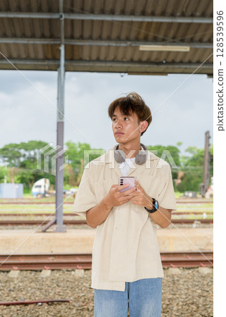 Young non binary tourist traveler in train station using phone 128539596