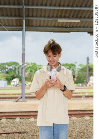 Young non binary tourist traveler in train station using phone 128539597