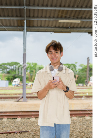 Young non binary tourist traveler in train station using phone Young non binary tourist traveler in train station using phone 128539598