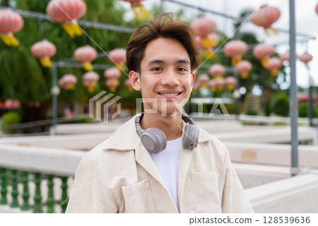 Asian non binary tourist person with headphones relaxing at park near lake 128539636