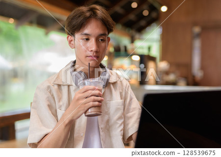 Handsome young non binary man sitting in cafe restaurant using laptop computer 128539675