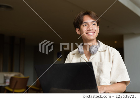 Non binary Asian student man sitting in modern coffee shop using laptop computer 128539723