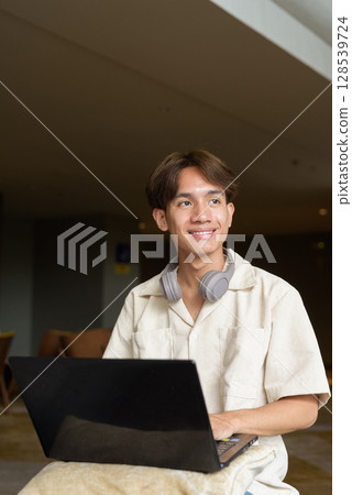 Non binary Asian student man sitting in modern coffee shop using laptop computer 128539724