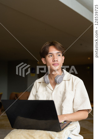Non binary Asian student man sitting in modern coffee shop using laptop computer Non binary Asian student man sitting in modern coffee shop using laptop computer 128539725
