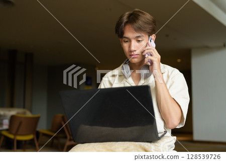 Non binary Asian student man sitting in modern coffee shop using laptop computer Non binary Asian student man sitting in modern coffee shop using laptop computer 128539726
