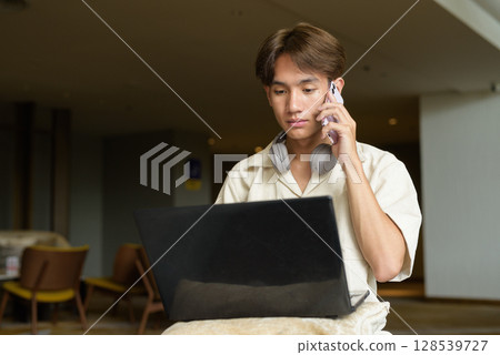 Non binary Asian student man sitting in modern coffee shop using laptop computer Non binary Asian student man sitting in modern coffee shop using laptop computer 128539727