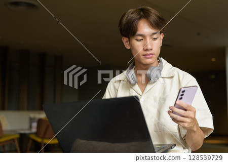 Non binary Asian student man sitting in modern coffee shop using laptop computer Non binary Asian student man sitting in modern coffee shop using laptop computer 128539729