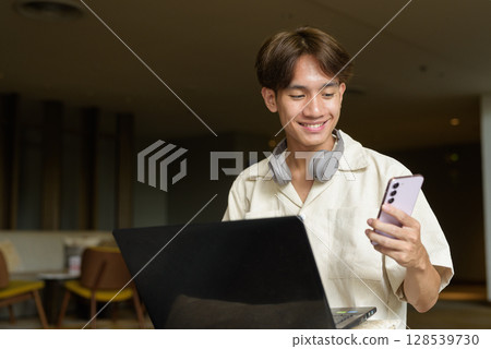 Non binary Asian student man sitting in modern coffee shop using laptop computer Non binary Asian student man sitting in modern coffee shop using laptop computer 128539730