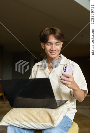 Non binary Asian student man sitting in modern coffee shop using laptop computer Non binary Asian student man sitting in modern coffee shop using laptop computer 128539731