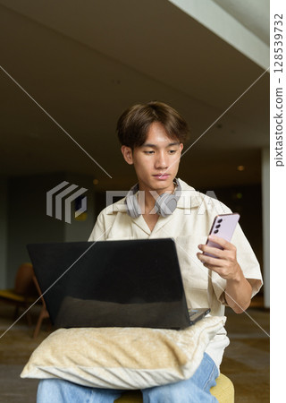 Non binary Asian student man sitting in modern coffee shop using laptop computer 128539732
