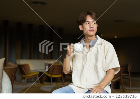 Non binary Asian student man sitting in modern cafe drinking coffee 128539736