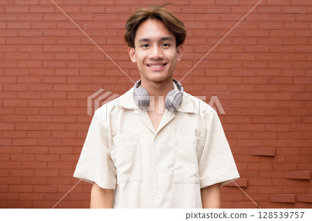Non binary cute Asian young gay man against brick wall 128539757
