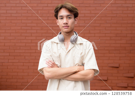 Non binary cute Asian young gay man against brick wall 128539758